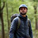 Ritratto di Simone Verdi, appassionato di trekking, con uno zaino leggero in un paesaggio boschivo